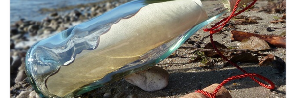 Eine Glasflasche mit einem Pergament am Strand, daneben ein Korken.